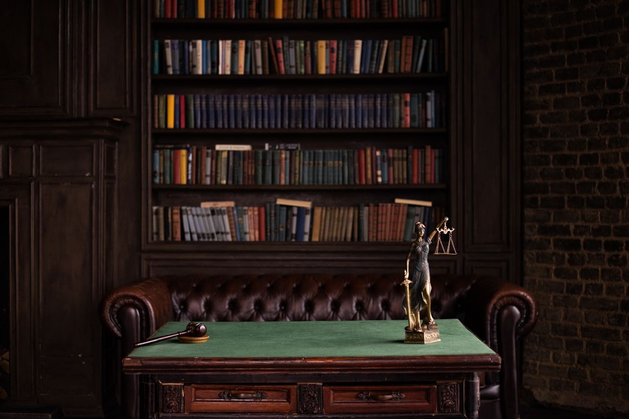 services-01 A classic study room with shelves of books, a gavel, and Lady Justice figurine on a green table.